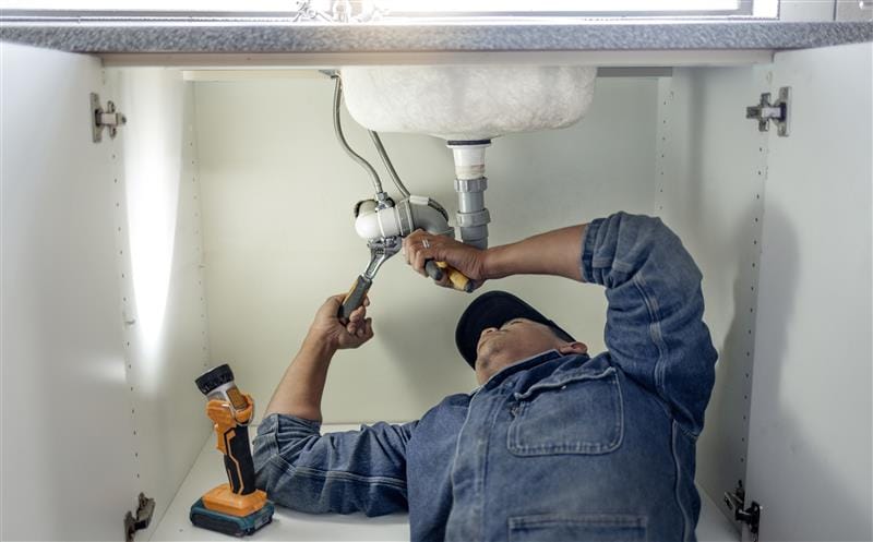 Plumber repairing pipes beneath a bathroom sink in Pacifica